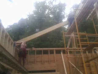 Carpenter raising a rafter beam on a new second story frame in Granville