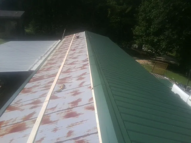 Old rusted panels beside newly installed green metal roofing — Wind Damage Roof Repair by Roofing Brothers in Granville